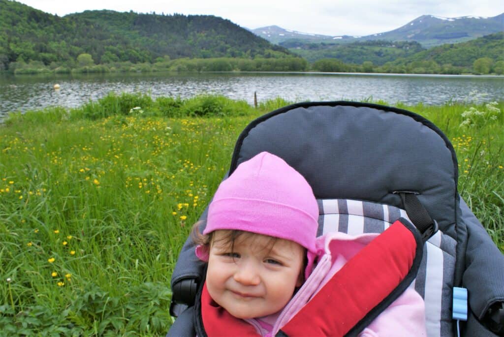 Baby in Kinderwagen vor Wiese, See, Hügeln und Bergen