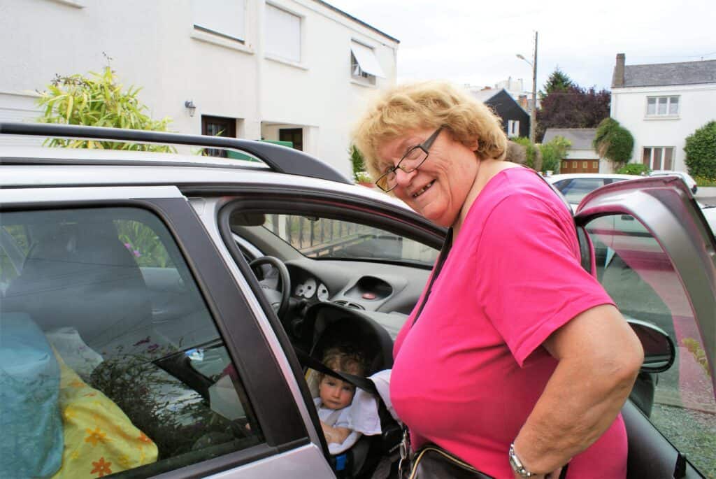 Vollbepacktes Auto mit Baby und etwa 70-jähriger Frau, die in die Kamera lächelt