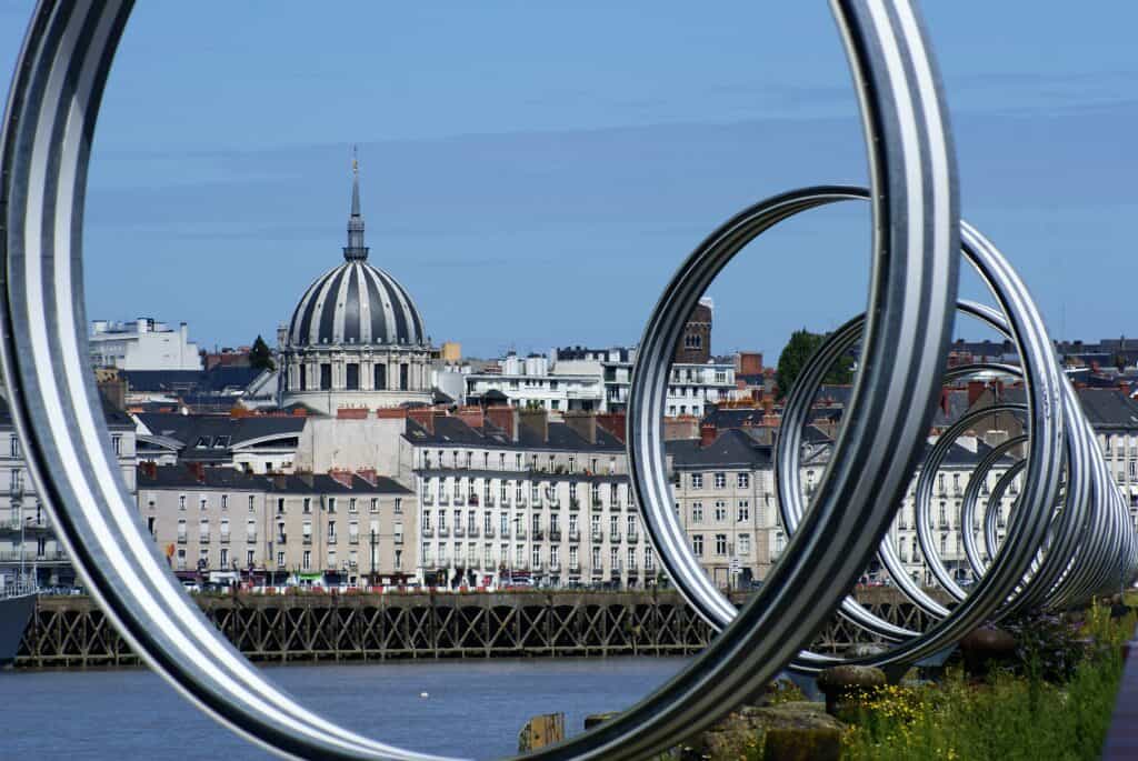 Kunstwerk aus mehreren großen Metallringen, dahinter Silhouette einer Stadt und ein Fluss