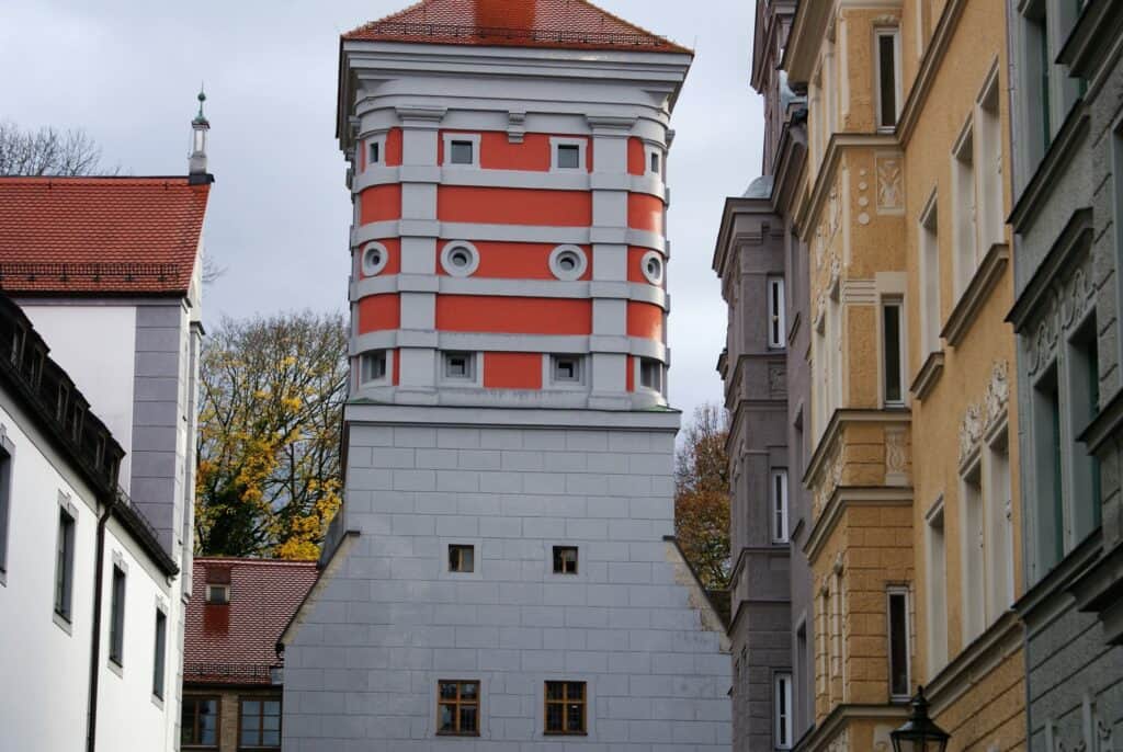 Straße in einer Altstadt mit verschieden farbigen Fassaden, am Ende der Straße ein Stadttor