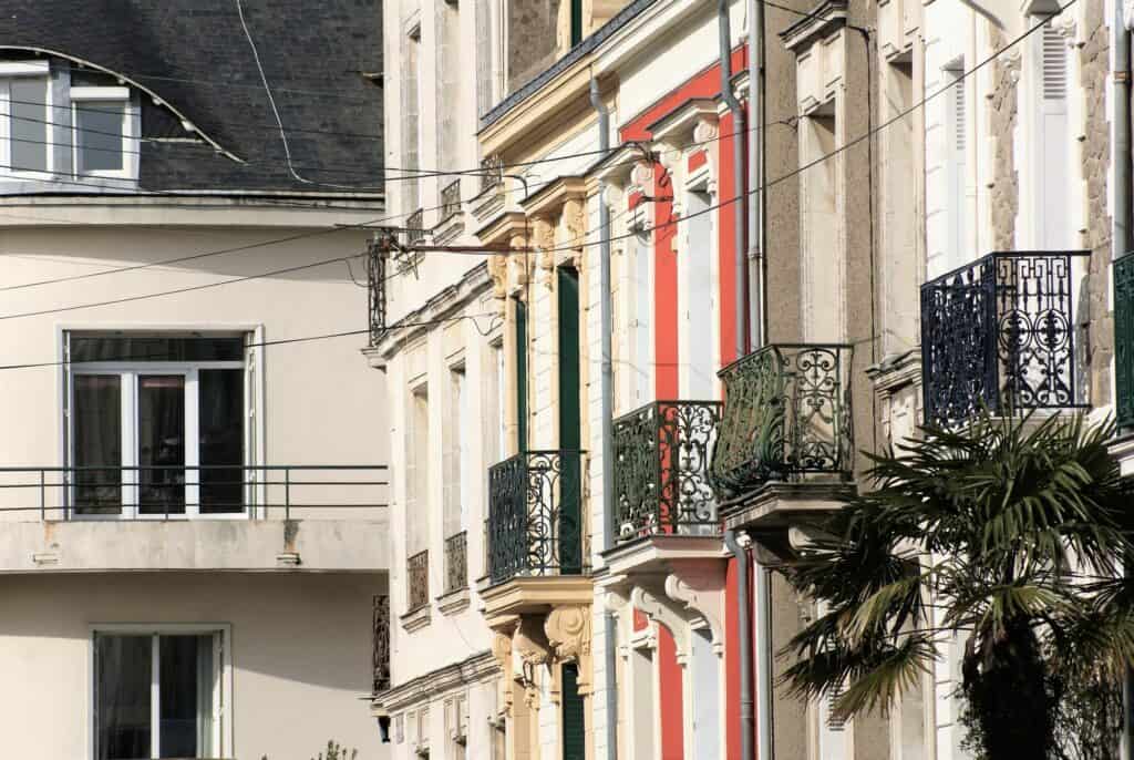 Mehrere Hausfassaden in verschiedenen Farben mit schönen alten Balkonen, im Vordergrund eine kleine Palme