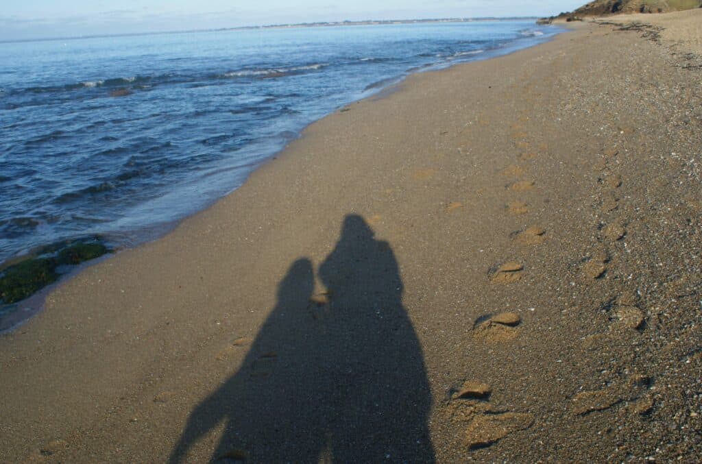 Links Meer, rechts nasser Sandstrand mit Fußabdrücken und dem Schatten von 2 Personen