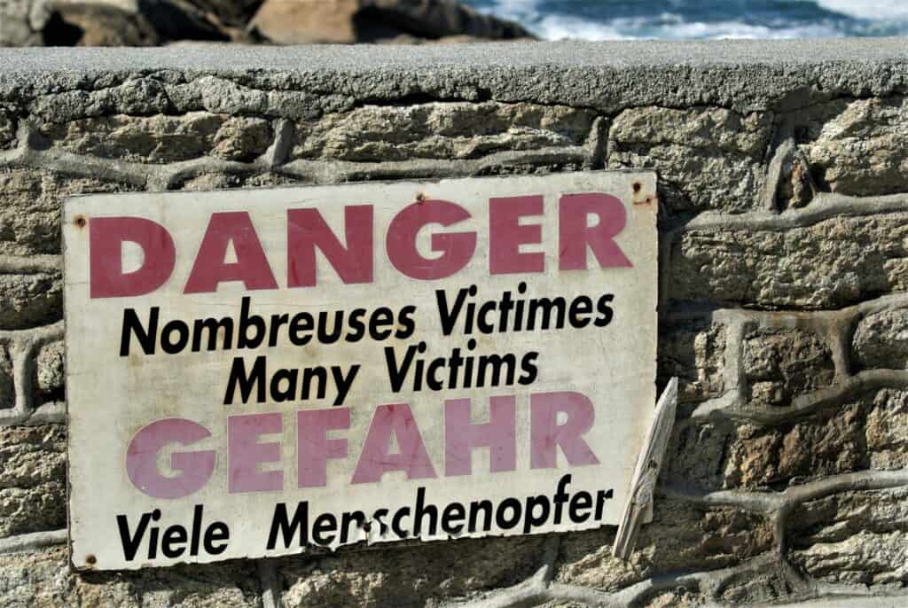 Schild an einer Mauer auf Französisch und Deutsch: Gefahr! Viele Menschenopfer! Hinter der Mauer der Atlantik