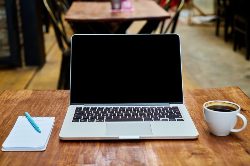 Schreibtisch mit Laptop, Notizblock und Tasse Kaffee
