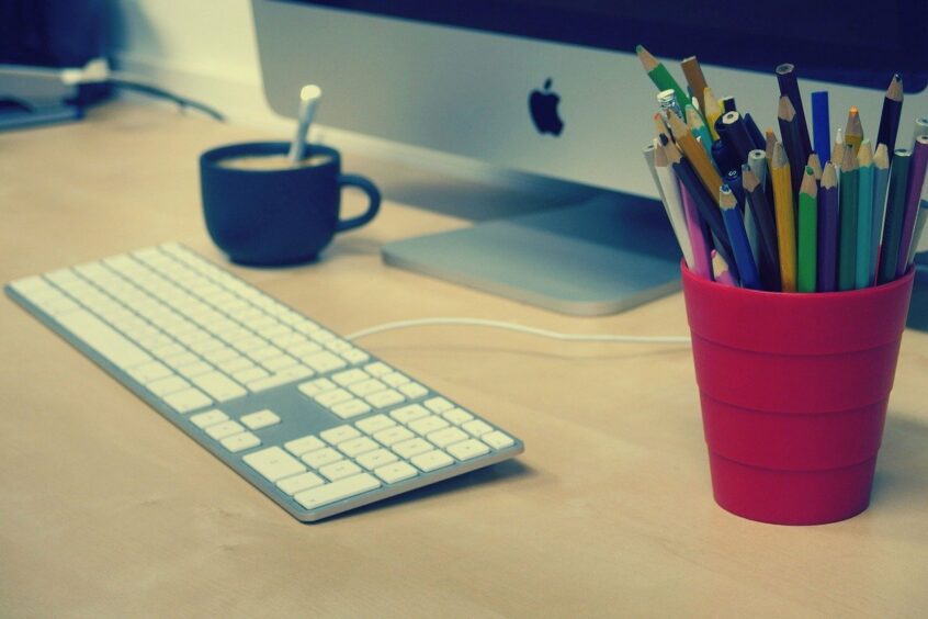 Schreibtisch mit Bildschirm, Tastatur, Stiften und Tasse Kaffee