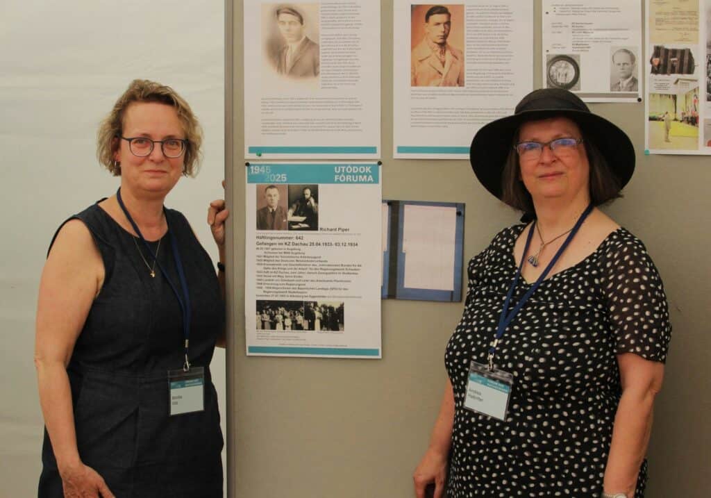 Zwei Frauen in scharzen Kleidern vor einer Stellwand mit Biografien
