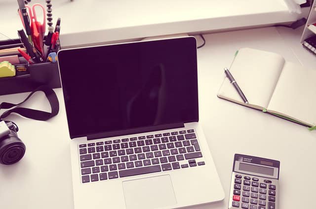Schreibtisch mit Laptop, Notizblock, Stift und Taschenrechner