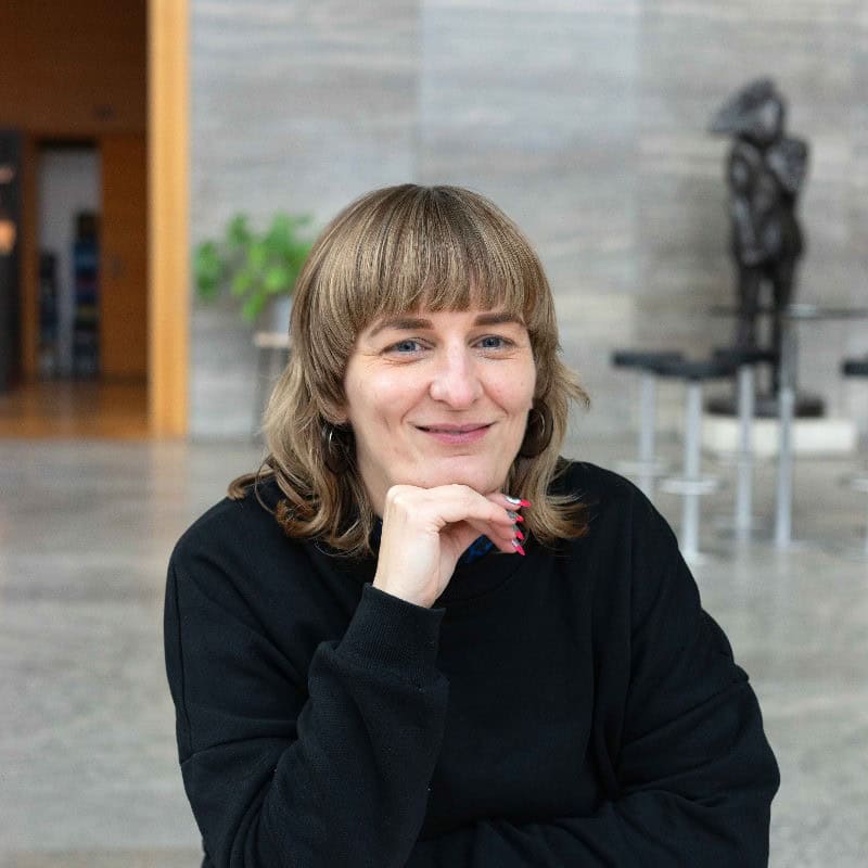 Miriam Grün mit schulterlangen blonden Haaren, blauen Augen und schwazrem Pullover