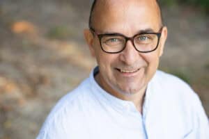 Mann mit hellem Hemd, Brille, grauen Augen und sehr kurzen Haaren