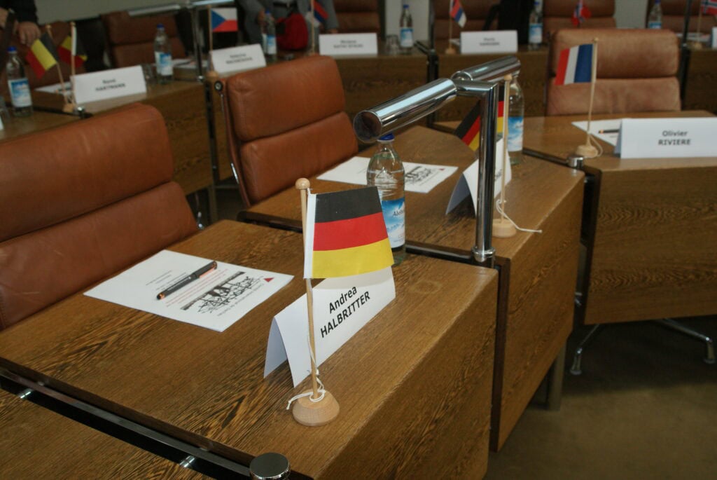 Konferenzraum mit Tischen aus Holz und Bürostühlen, vorne zwei kleine deutsche Flaggen und ein Schild mit der Aufschrift Andrea Halbritter
