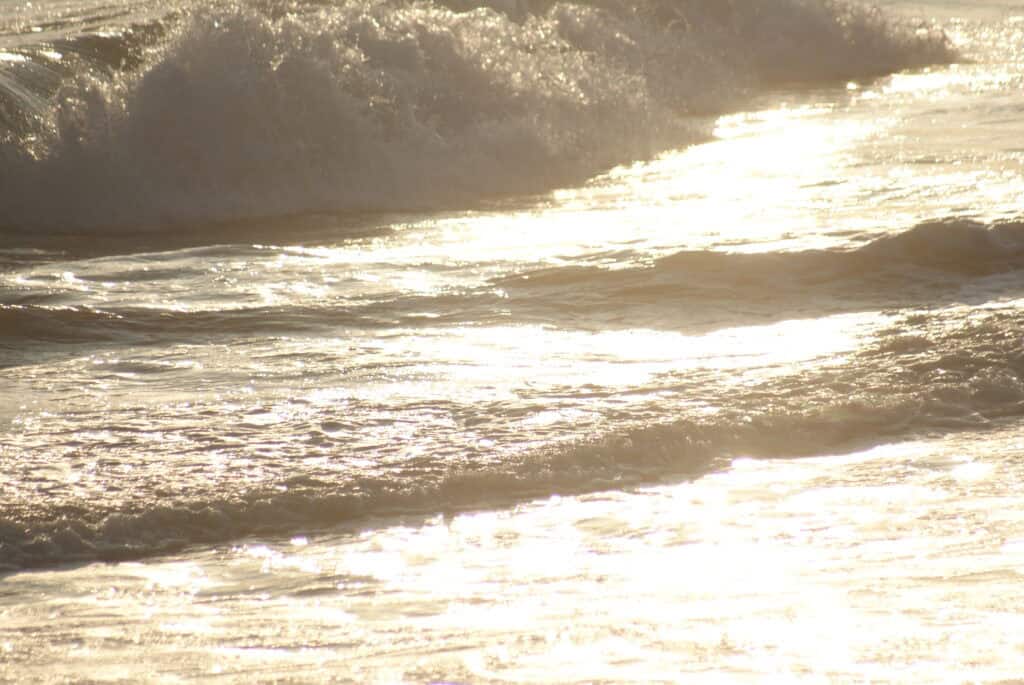 Sandstrand mit leichten Wellen in silbernem Sonnenlicht