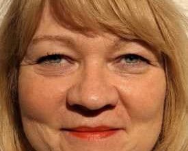 Lächelnde, ältere Frau mit kinnlangen blonden Haaren, blaugrauen Augen, schwarzer Wimperntusche und Lippen mit rotem Lippenstift