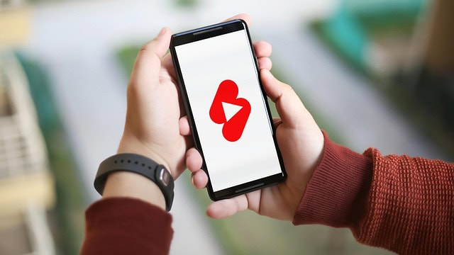 Zwei Hände halten ein Smartphone, auf dem das Logo von YouTube zu sehen ist